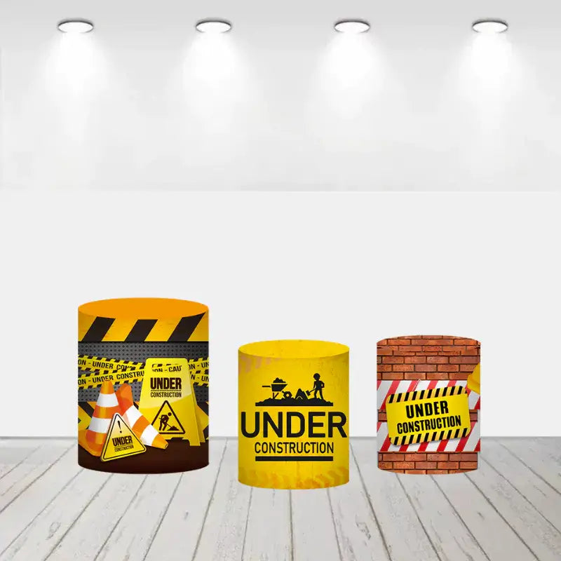 Three construction-themed cylinder covers: one with caution cones and signs, another with a bold yellow "Under Construction" print, and the third styled as a brick wall with a caution banner.