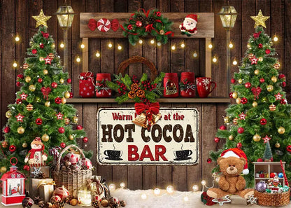 Holiday photo backdrop with a "Hot Cocoa Bar" sign, Christmas trees, and festive decor