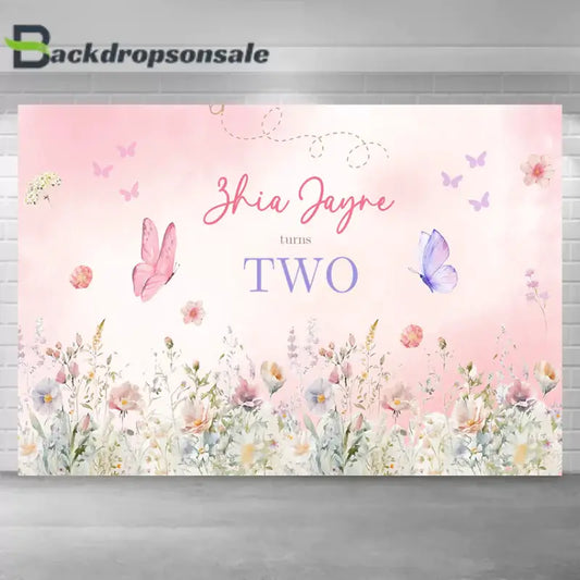 Floral and butterfly-themed second birthday backdrop featuring delicate flowers, pastel butterflies, and the text 'Zhia Jayne turns Two.'