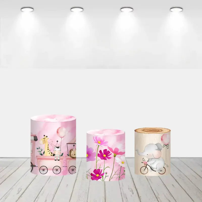 Three pink safari-themed cylinder covers: one featuring safari animals on a train, another with blooming pink flowers, and the third showing an elephant riding a bicycle with balloons.