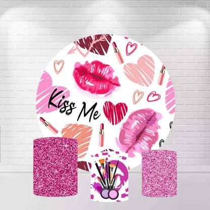 A "Kiss Me" themed party decor set featuring a large round backdrop with pink and red lipstick kiss prints, hearts, and lipsticks, alongside three matching cylinder covers with pink glitter and makeup brush designs.