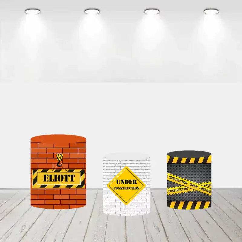 Set of three cylinder covers, one with a brick wall and crane hook, another with a white brick wall and "Under Construction" sign, and the third with caution tape design.