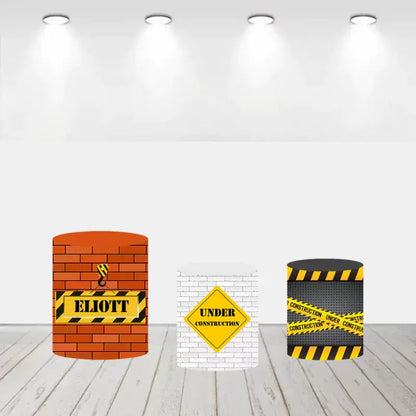 Set of three cylinder covers, one with a brick wall and crane hook, another with a white brick wall and "Under Construction" sign, and the third with caution tape design.